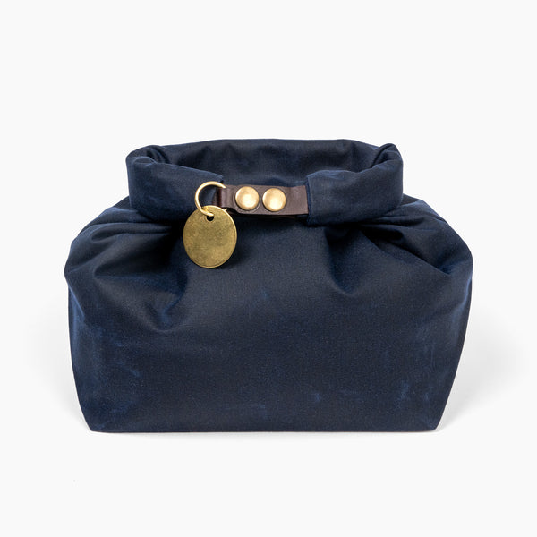 Closed medium navy blue waxed canvas roll top stuff sack with leather closure and brass tag 