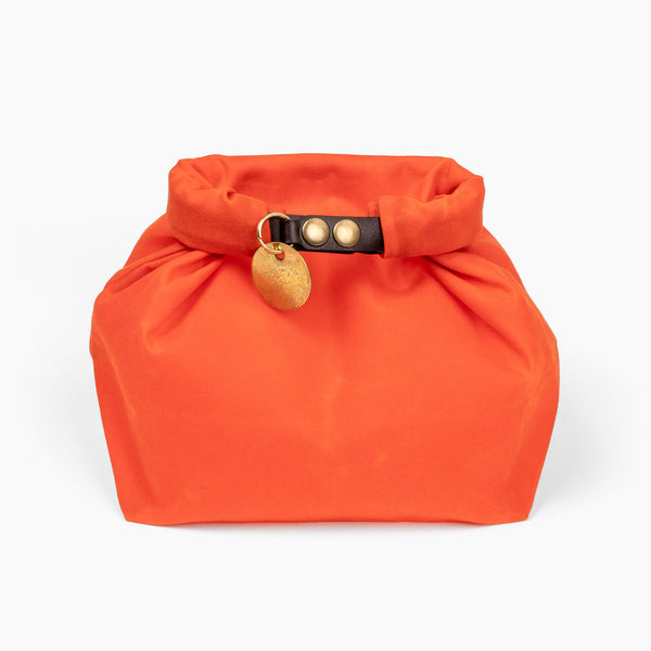 Closed medium hunter orange waxed canvas roll top stuff sack with leather closure and brass tag 